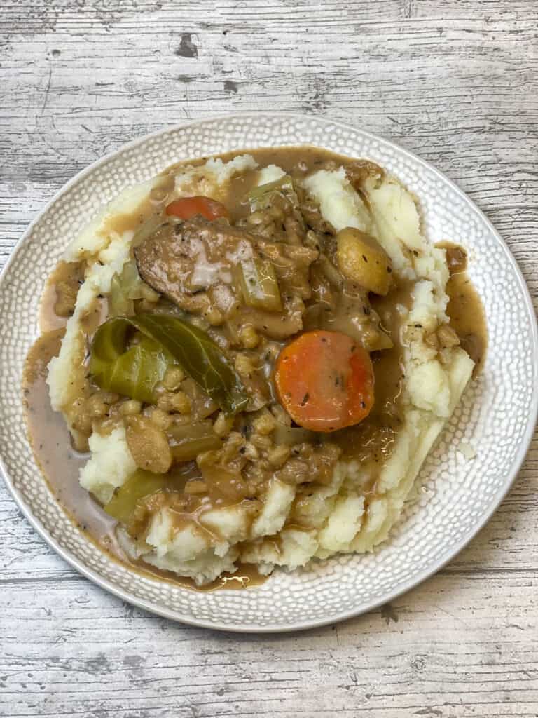 creamed vegan beef and barley stew served on white plate with mashed potatoes, white wooden background.