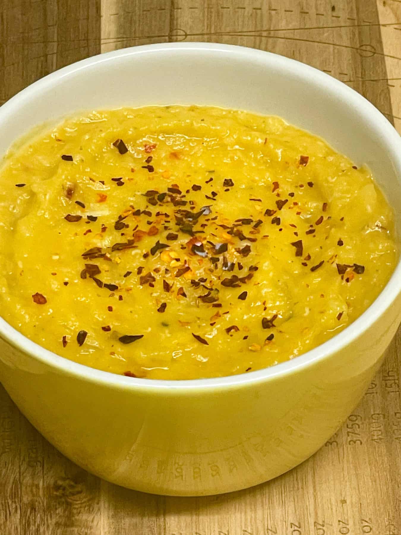 Small yellow bowl filled with lentil-pumpkin pate with red pepper flakes.