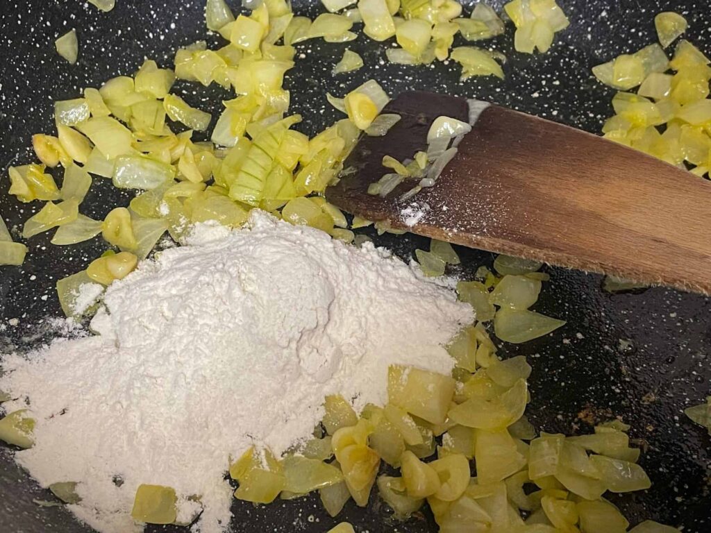 flour added to cooking onions in pan, wooden spatula to side.