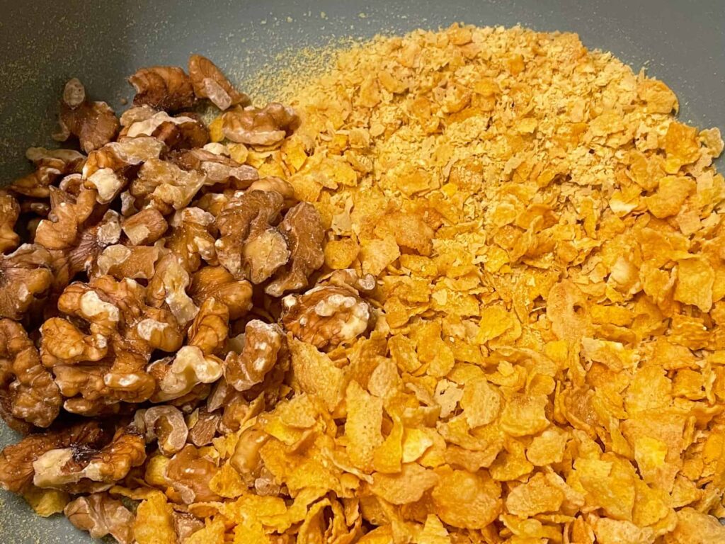 cornflakes, walnuts and nutritional yeast flakes added to turquoise coloured mixing bowl.