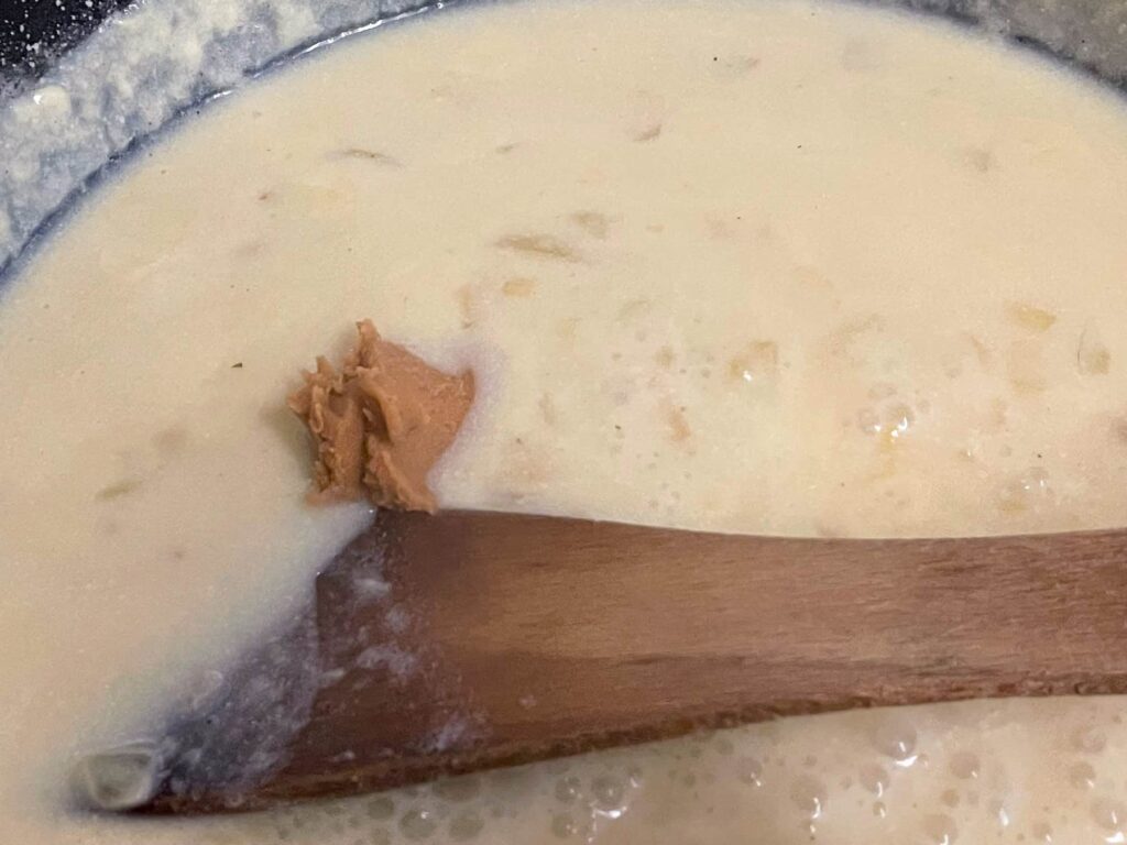 miso paste added to white sauce in pan being stirred with wooden spatula.