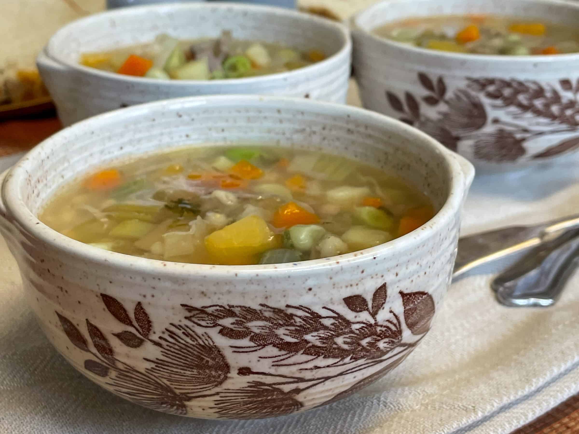 Close up of bowl of  hotchpotch, two bowls behind, bowls have brown wheat leaf pattern.