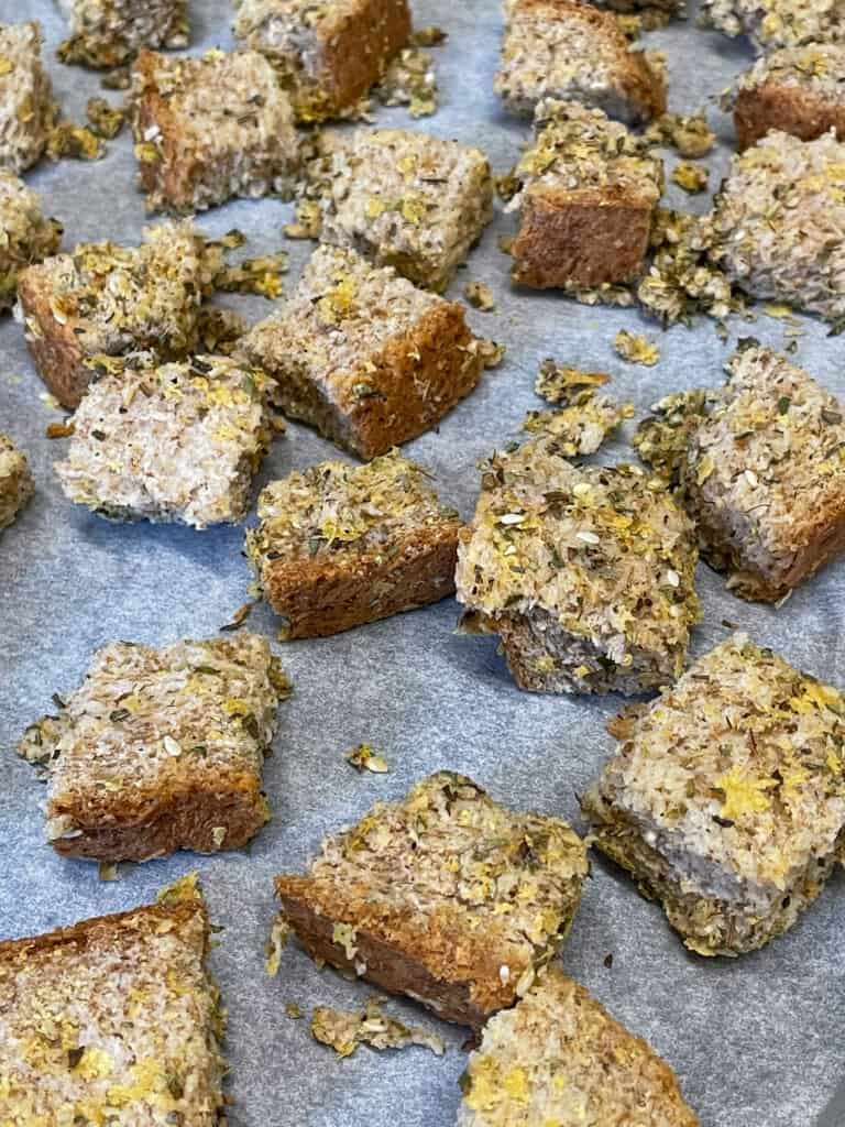 wholemeal bread cubes on baking tray with seasonings mixed through, ready to bake.