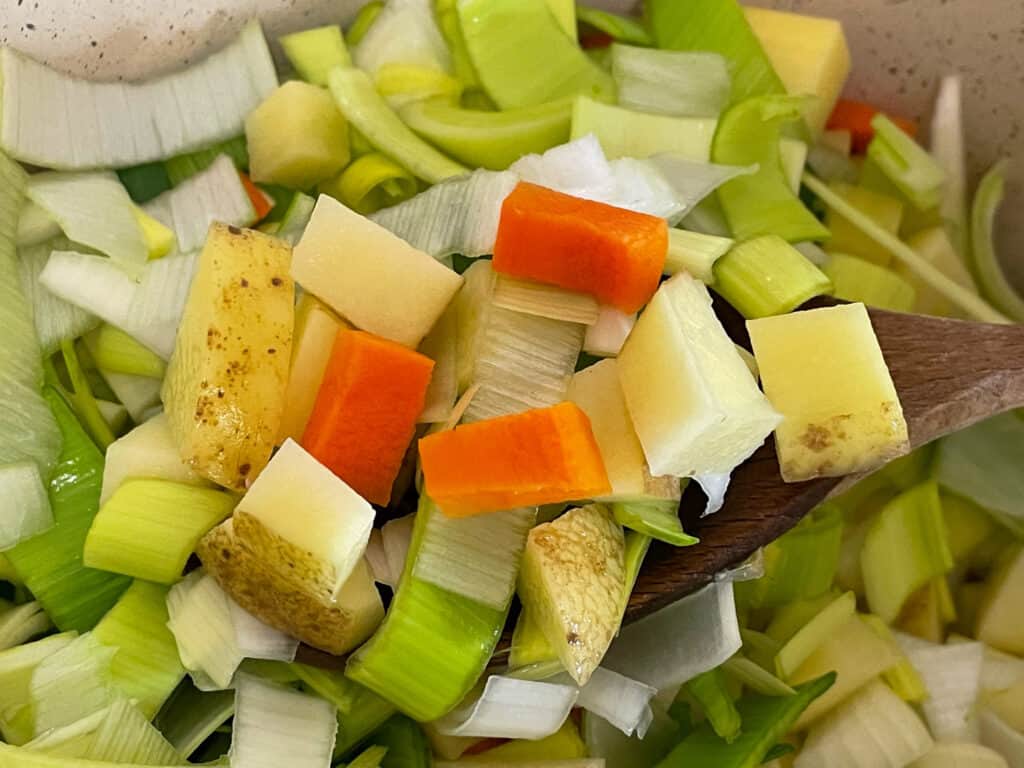 potato and leek veggies sliced and chopped in cooking pot.