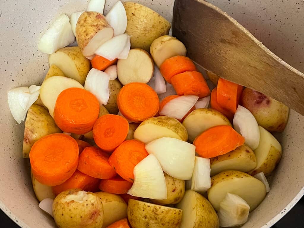 chopped potatoes, carrots and onion in pan with wooden spatula.