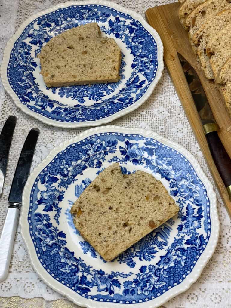 Slices of peanut butter bread on vintage blue and white patterned plates with white handled cutlery to side, wooden board with rest of peanut bread to side with chopping knife.