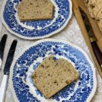 Slices of peanut butter bread on vintage blue and white patterned plates with white handled cutlery to side, wooden board with rest of peanut bread to side with chopping knife.