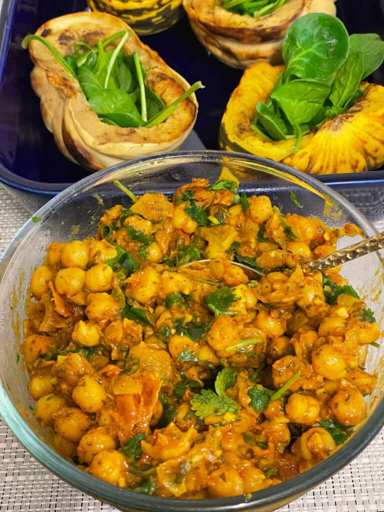 baked squash in a blue casserole dish with spinach in each squash, glass bowl of chana chaat to front of photo.