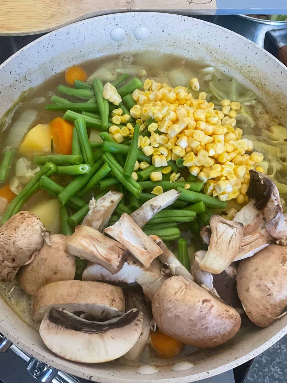 Mushrooms, green beans and sweet corn added to vegetable stew pot.
