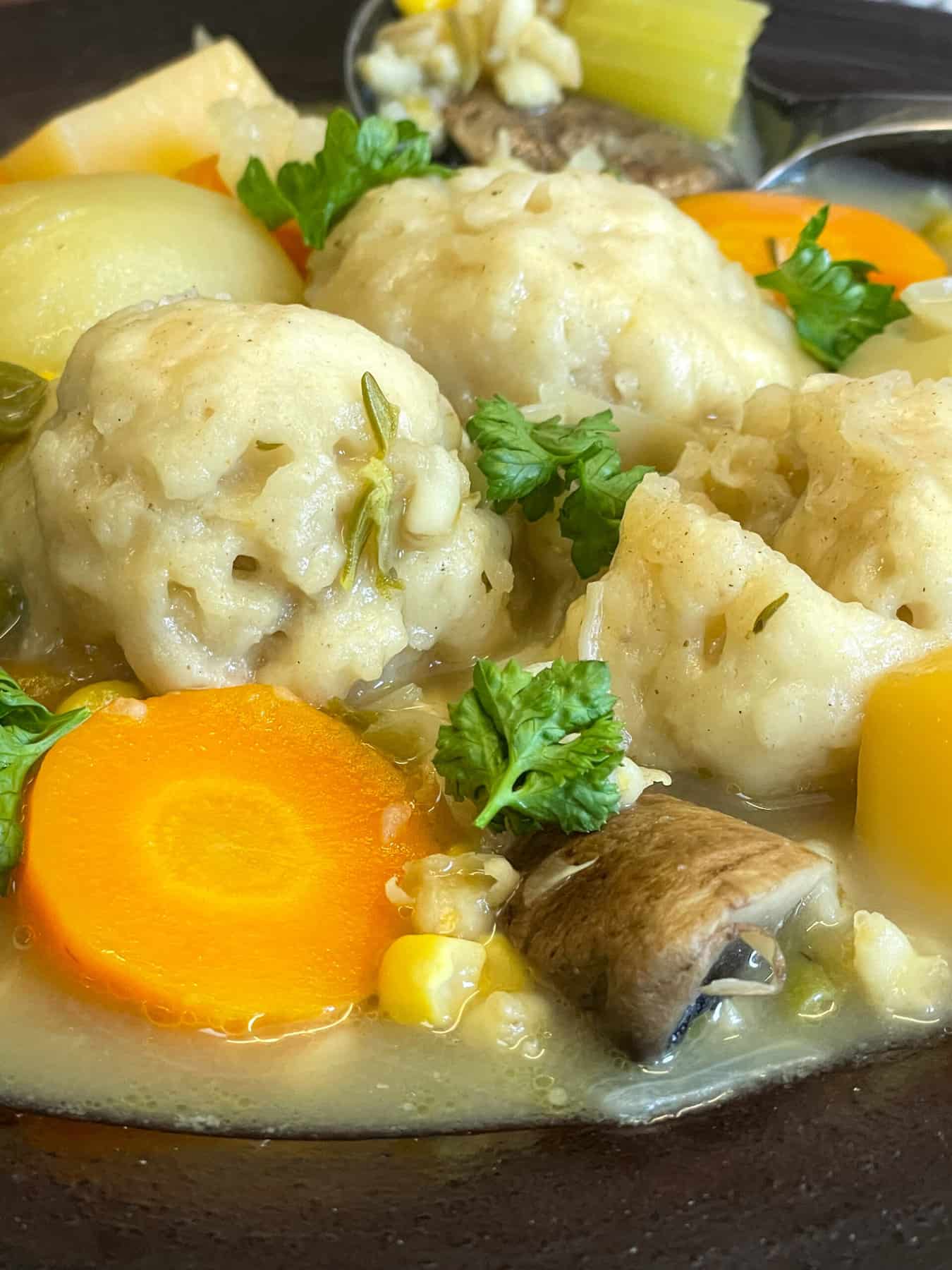 A bowl of vegetable stew with a spoon full in background.