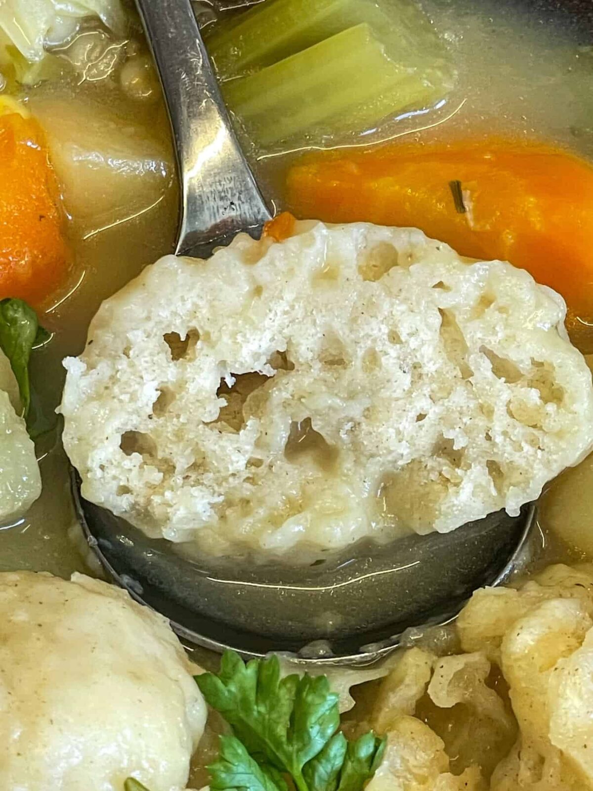 Cooked dumpling sliced in two to show the fluffy airiness of the insides, on a soup ladle.