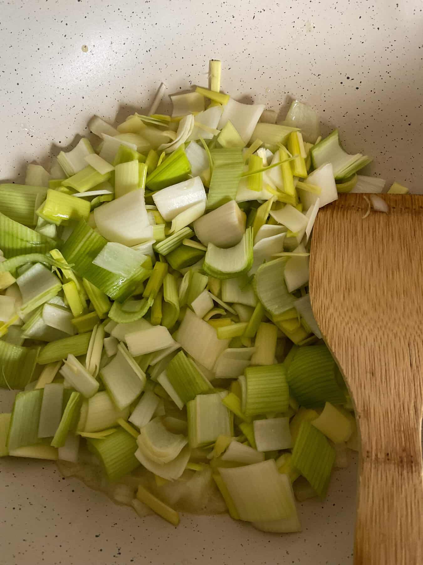 Cooking onions and leeks in pan with wooden spatula.