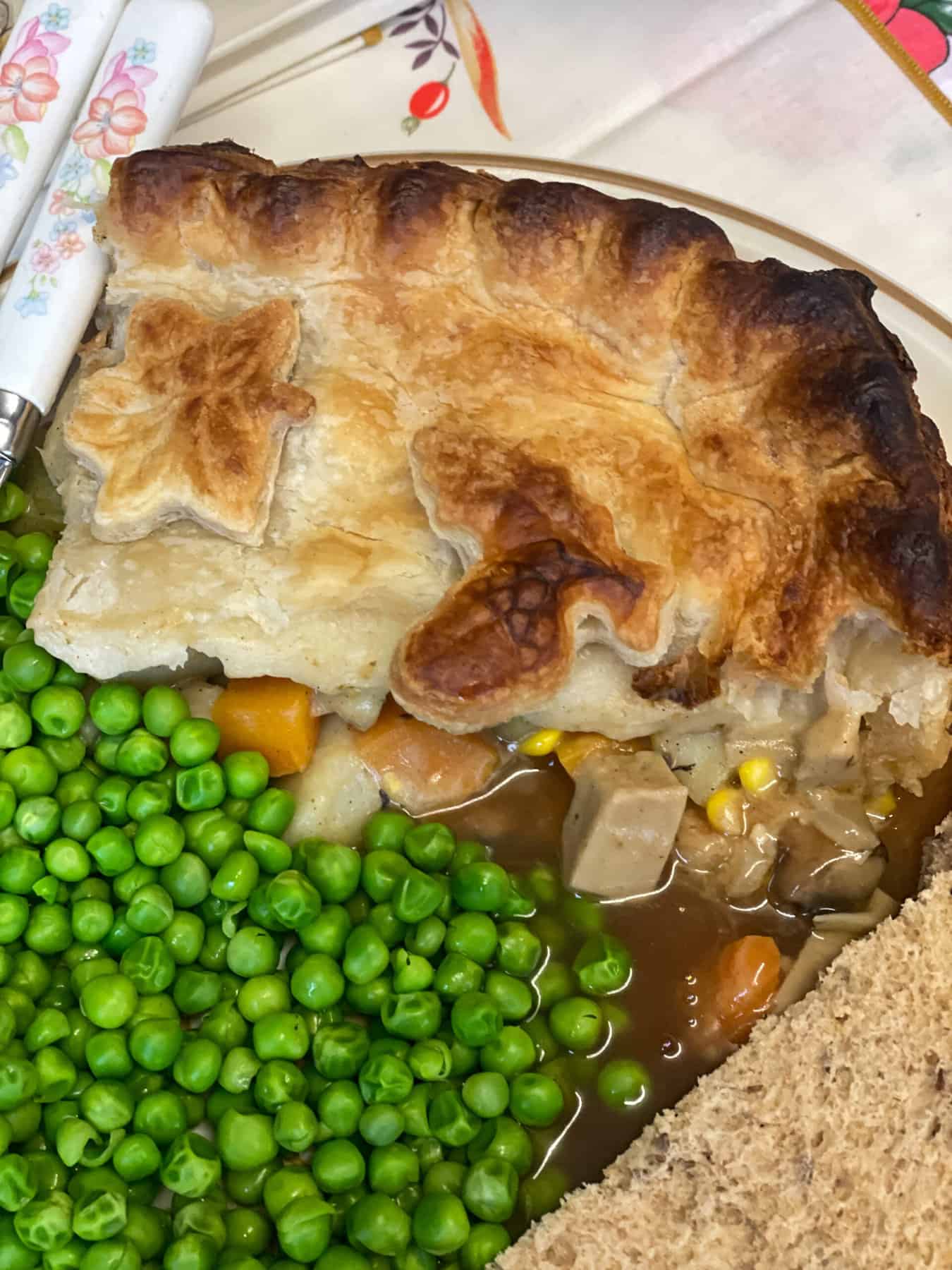 A slice of pie with a serving of green peas, wholemeal bread, and gravy.