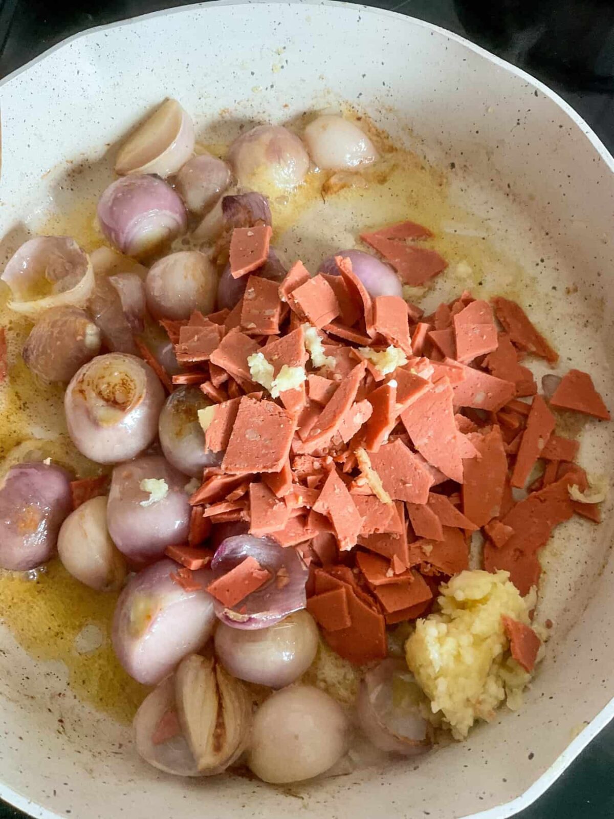 Vegan bacon pieces and crushed garlic added to pan with shallots.