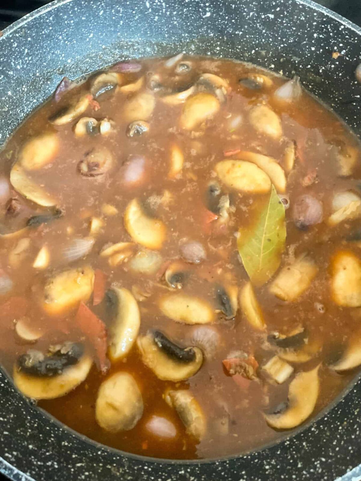 Liquids for sauce added to pan with coq au vin ingredients cooking.