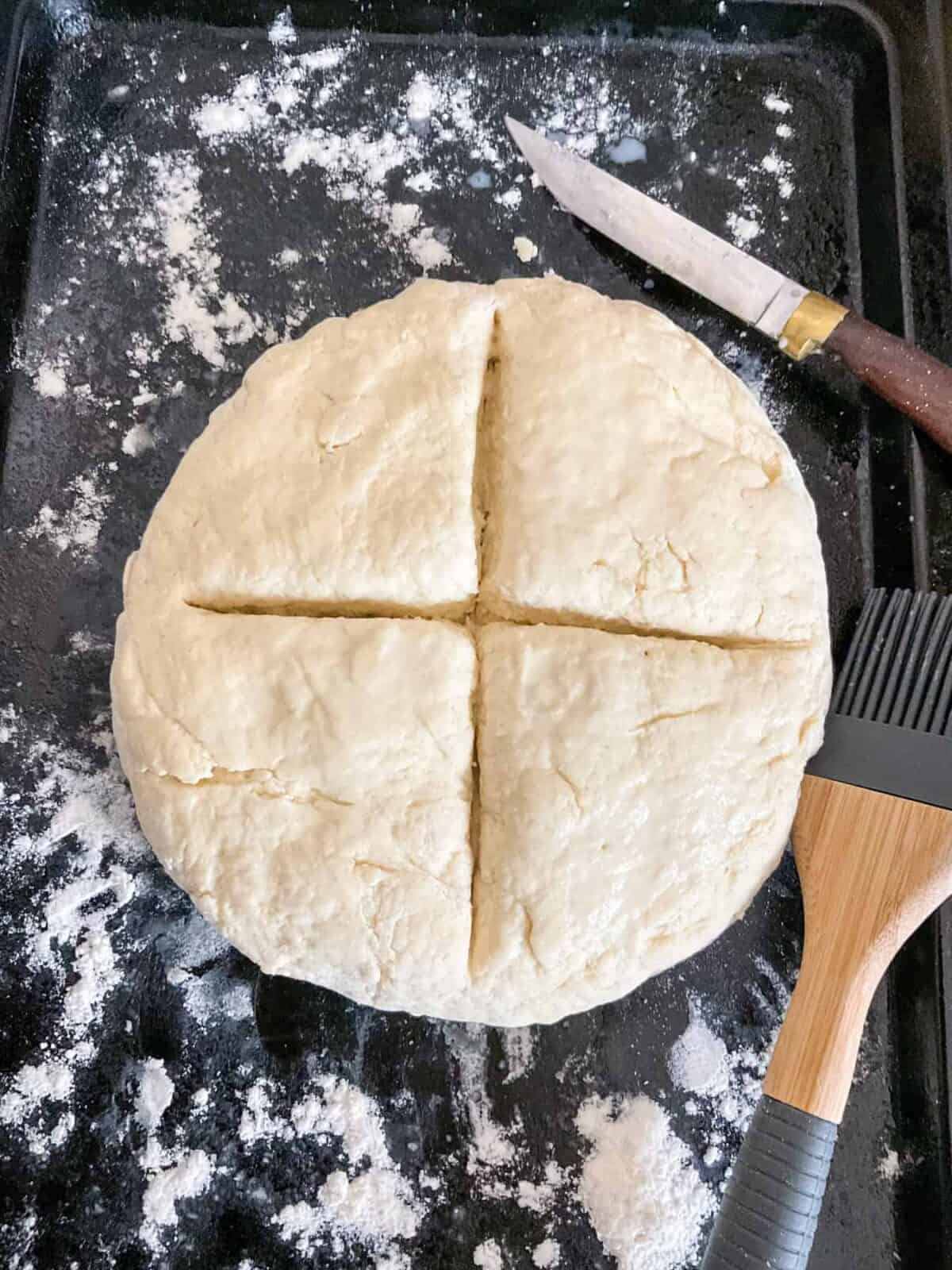 Bread with a deep cross scored through, knife to side and pastry brush to side.