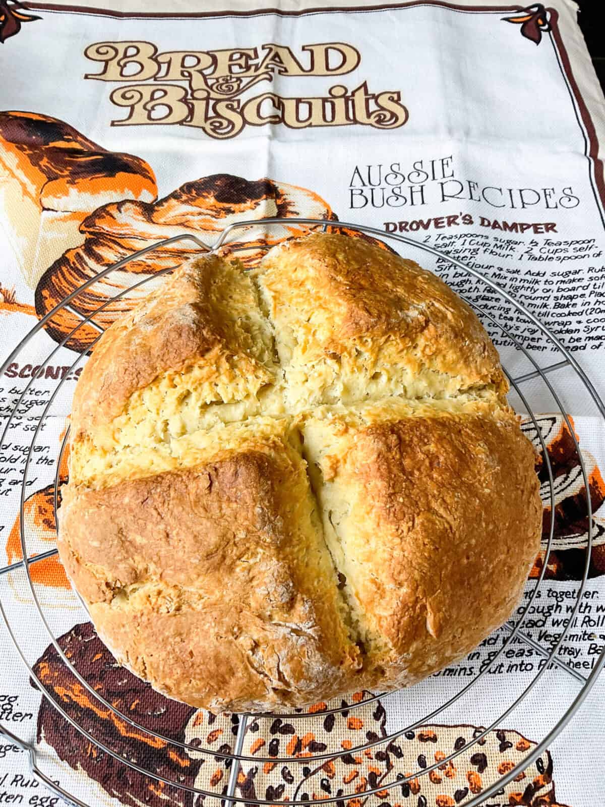 A loaf of damper bread on a wire rack with an Australian tea towel background.