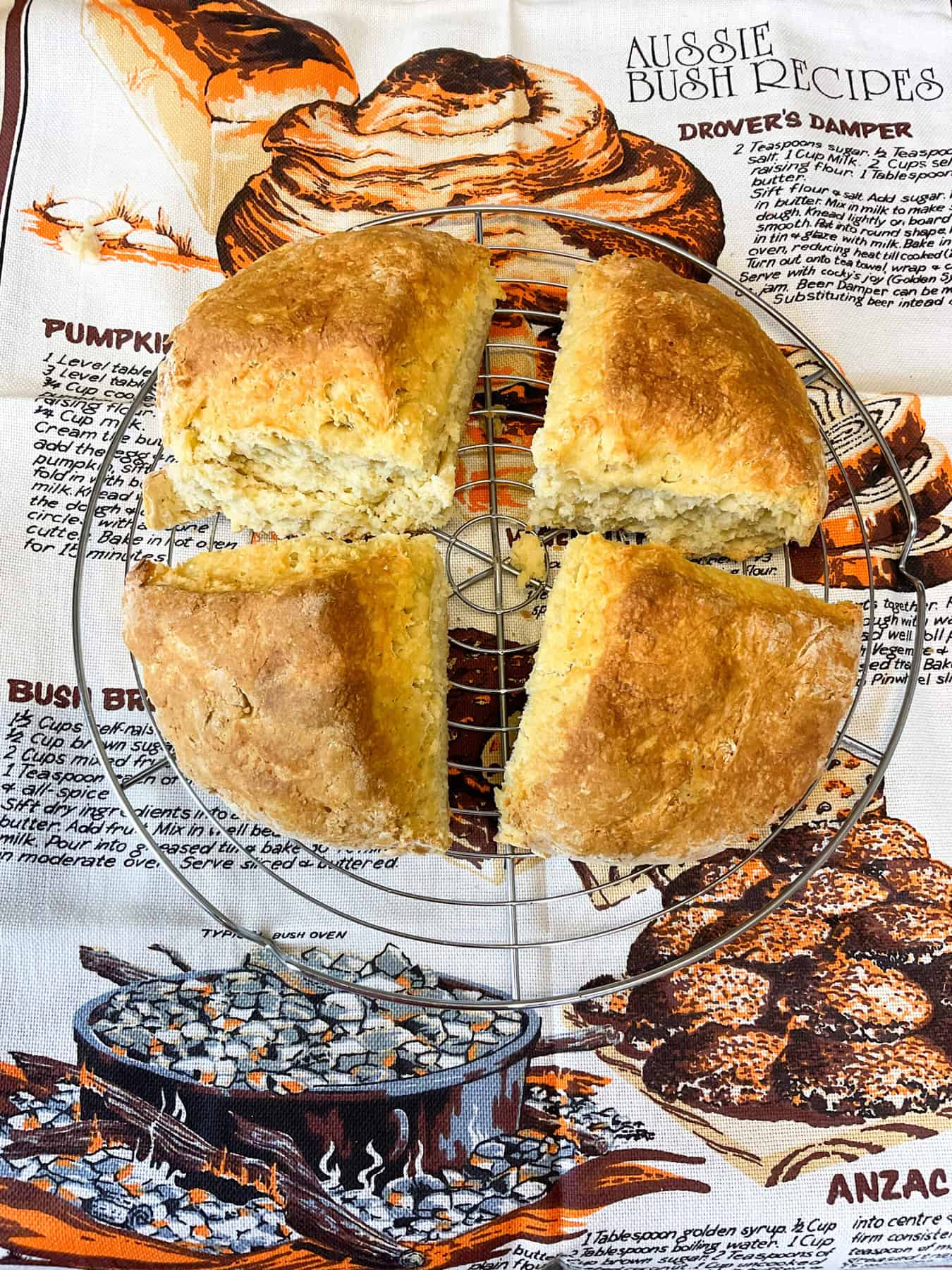Damper bread that has been pulled apart into 4 triangles with an Australian recipe tea towel in background.