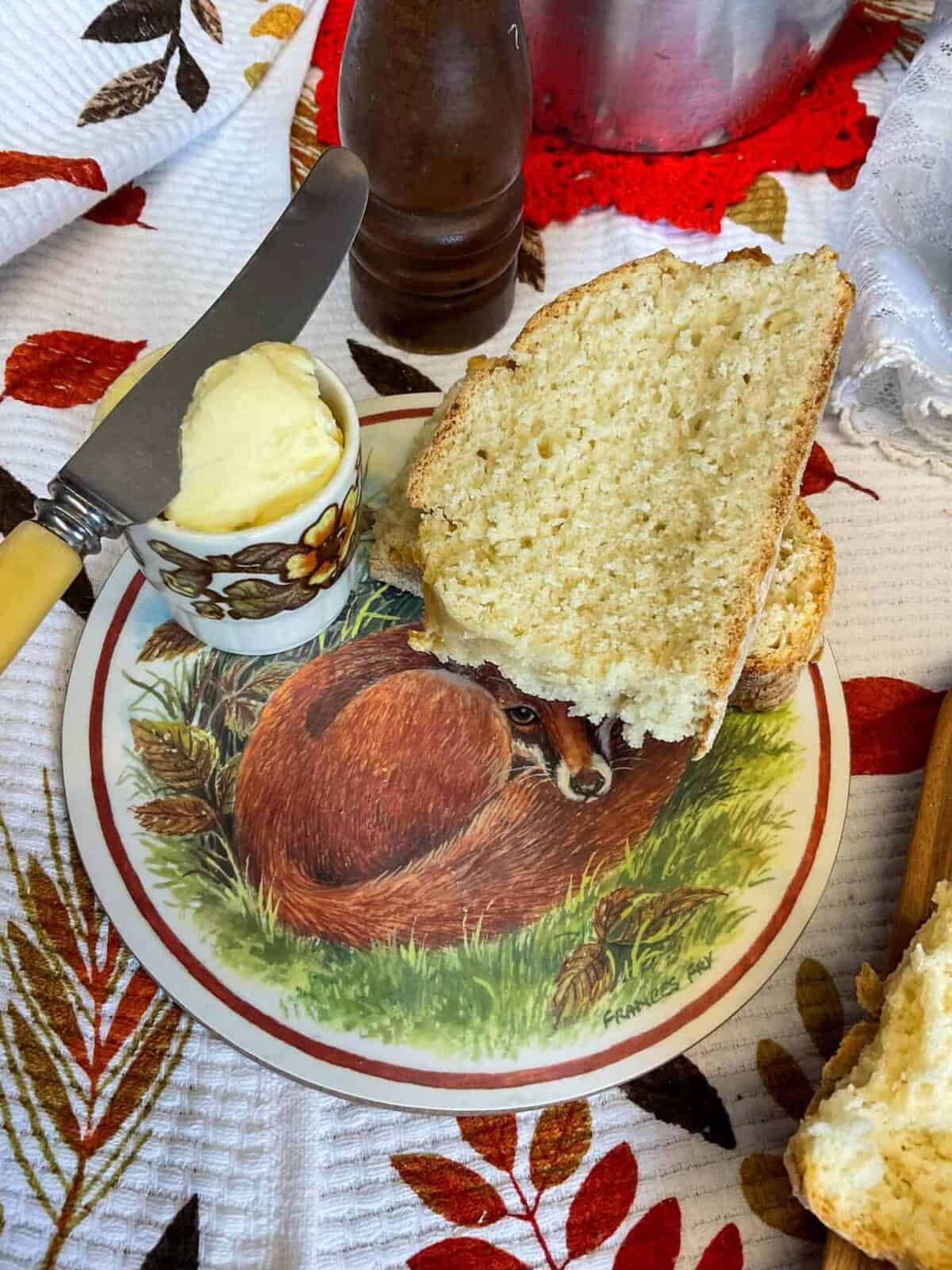 Two thin slices of damper bread on a wooden board with an image of a fox, butter knife to side, and a tea towel with leaf pattern in background.