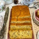 Vegan seed cake on a vintage tray with pink flower pattern, antique cake knife to side, flower patterned teapot, sugar dish, milk jug, and tea cup and saucer to side, crochet tablecloth background.