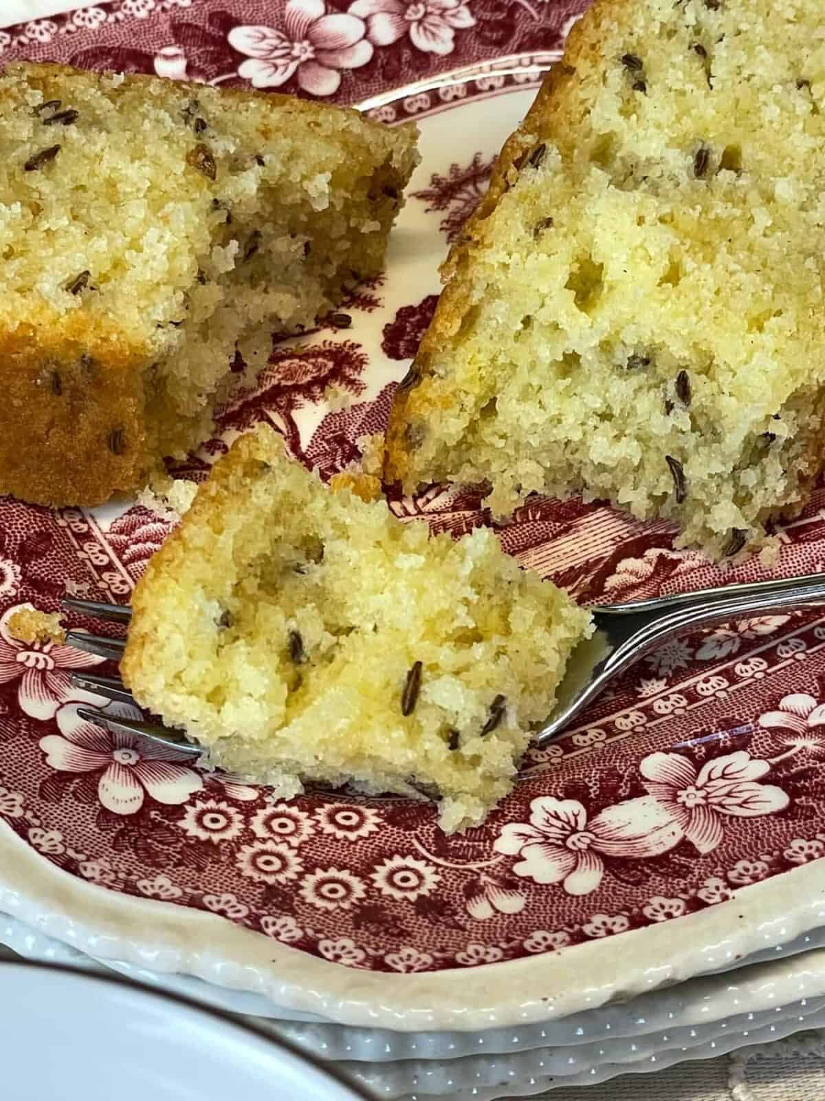 Small piece of seed cake on a cake fork with larger slice of cake to side on cake plate.