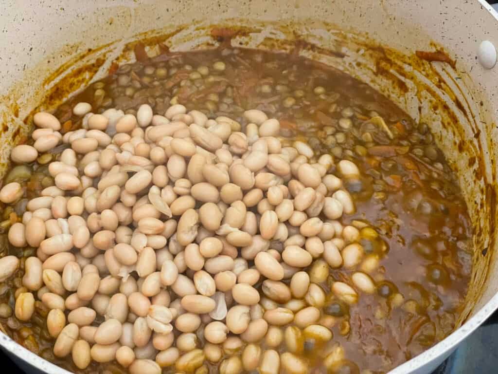 Haricot beans added to cooked lentils in pot.