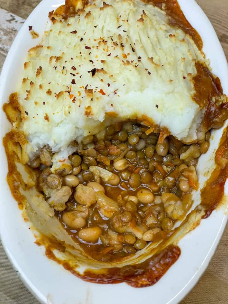 close up green lentil and bean mashed potato pie in a white oval pie dish.