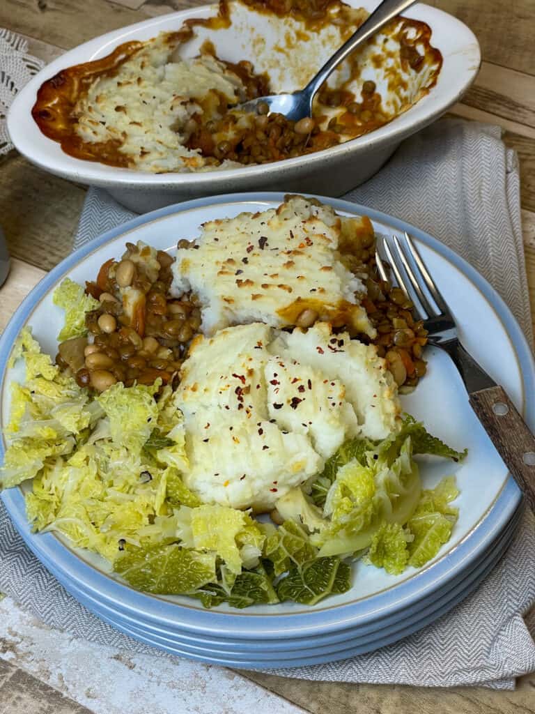 mashed potato pie served on light blue plate with steamed cabbage, pie dish to side, wooden table background.