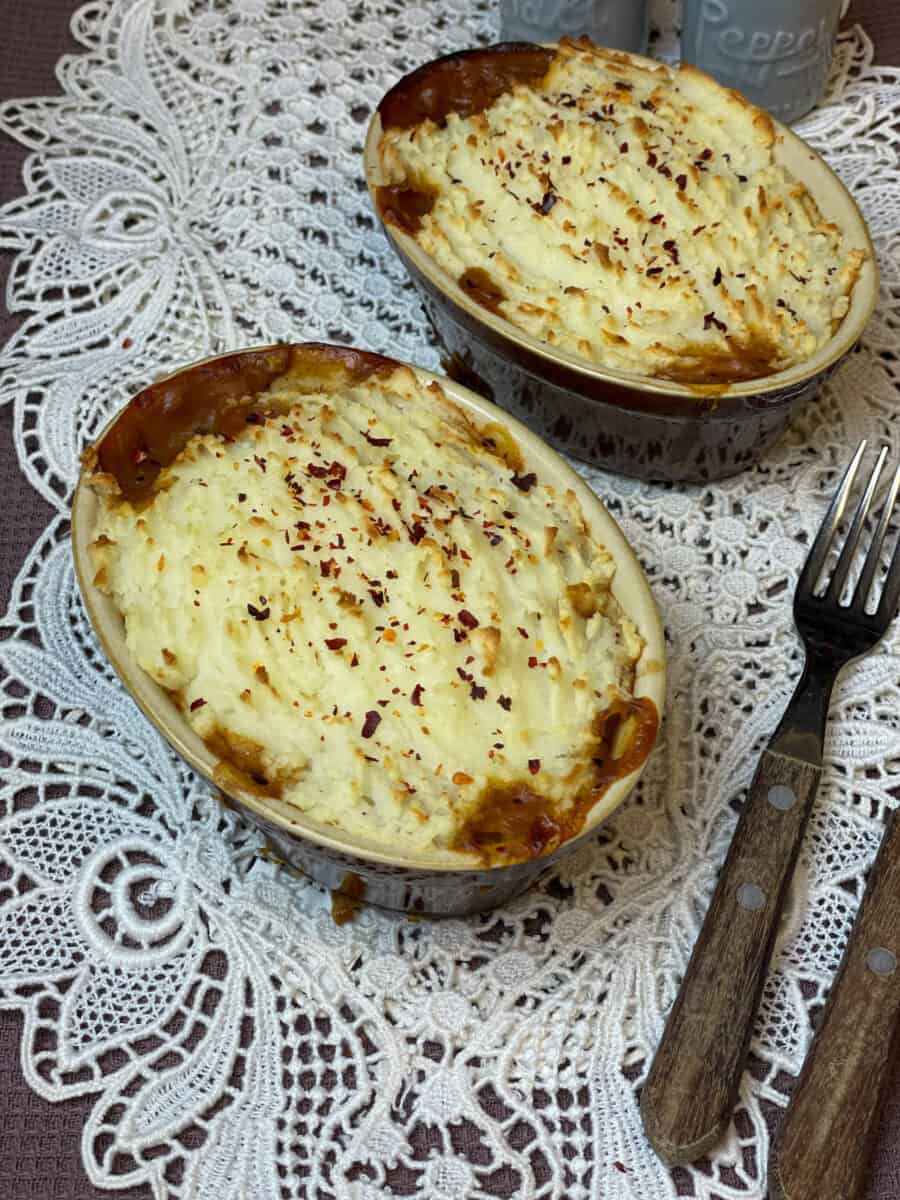 Two pie dishes of lentil and bean pie with fork to side and white doily background.