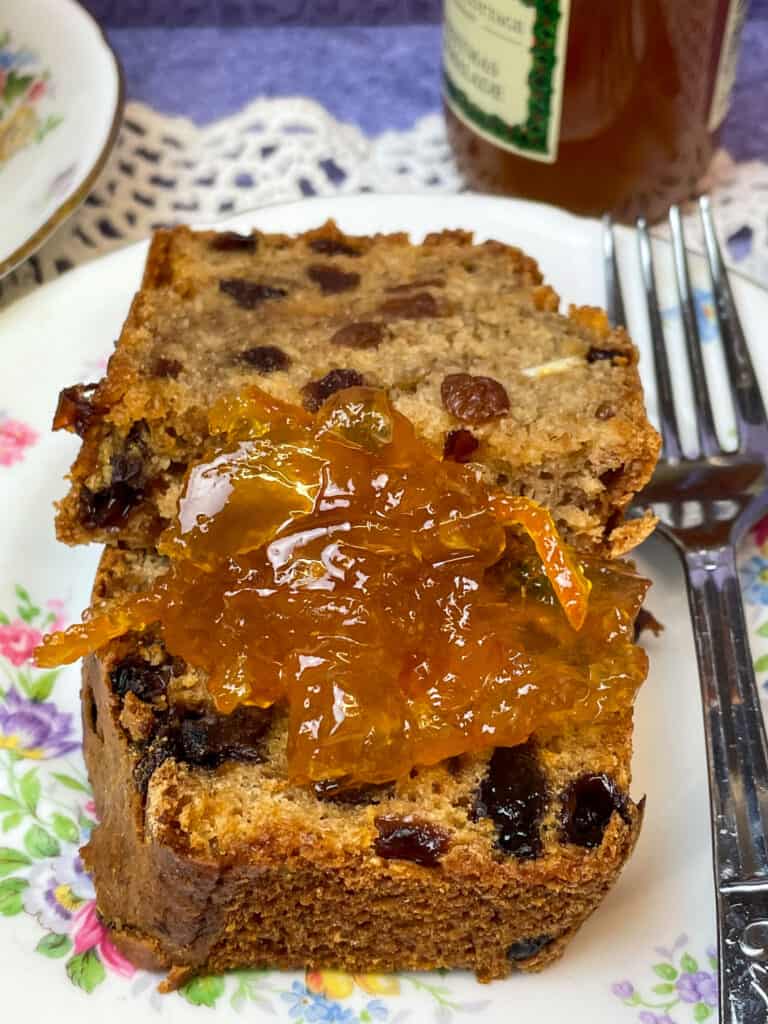 A dollop of marmalade on a slice of cake with cake fork to side, marmalade jar to side, and frilly placemat with purple background.