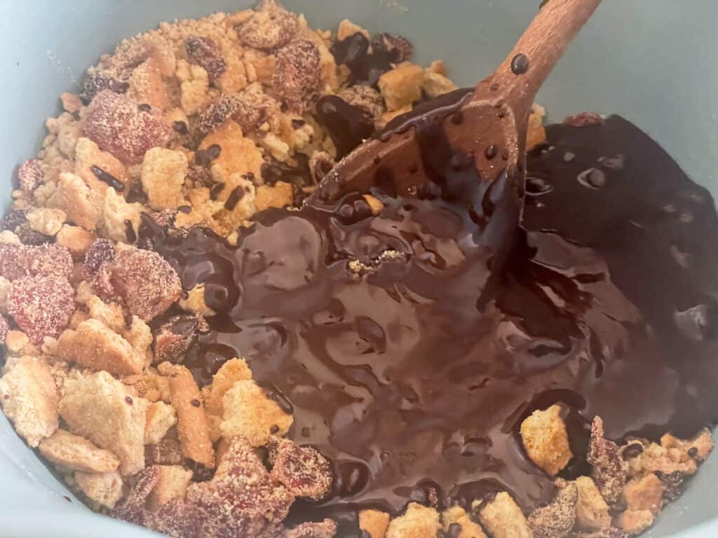 melted chocolate mix poured into crushed biscuit mix in bowl and stirred with wooden spoon.