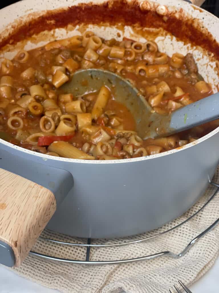 vegan one-pot American goulash ready to serve with grey ladle and the pot sitting on circle wire cooling rack on the dinner table.