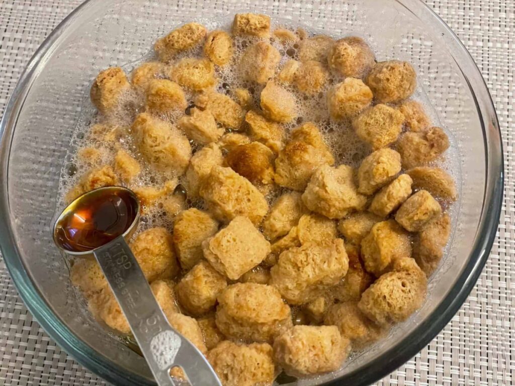 Soya chunks soaking in boiling water to rehydrate in a glass bowl with teaspoon.