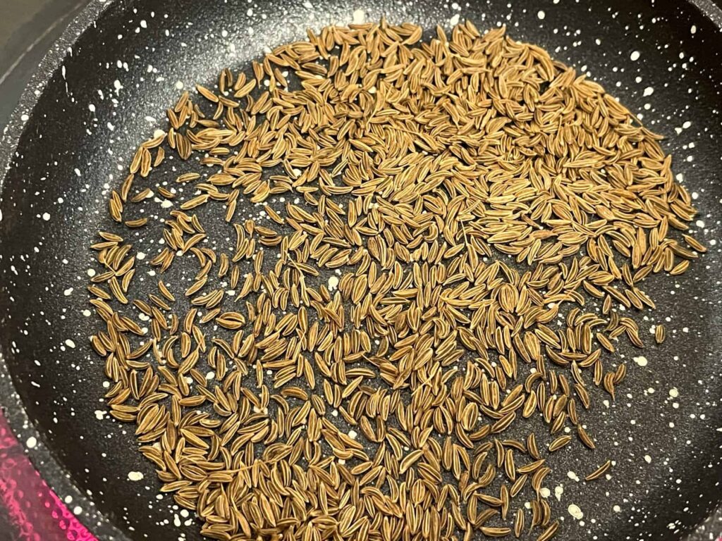 Caraway seeds in mini fry pan toasting over heat.