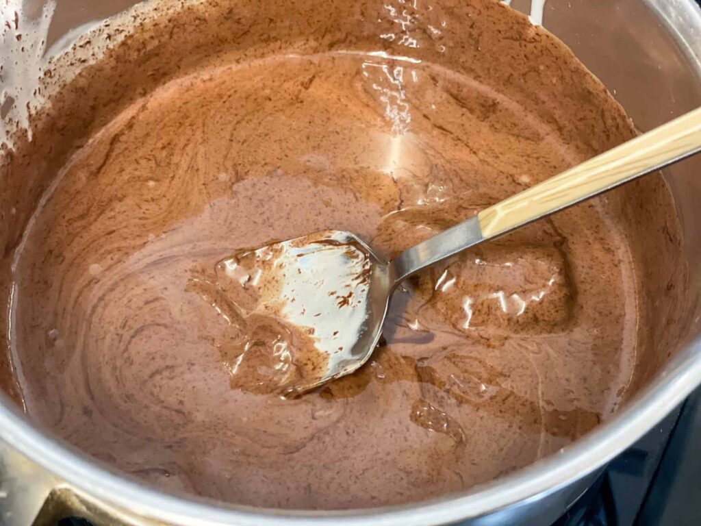 dark chocolate melted and being stirred into the cream with a sliver spoon with tan handle.