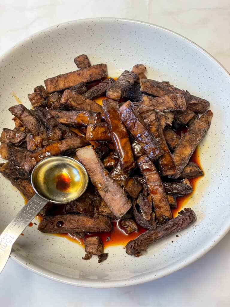 no beef strips marinading in cream coloured bowl with tablespoon measurer in bowl.