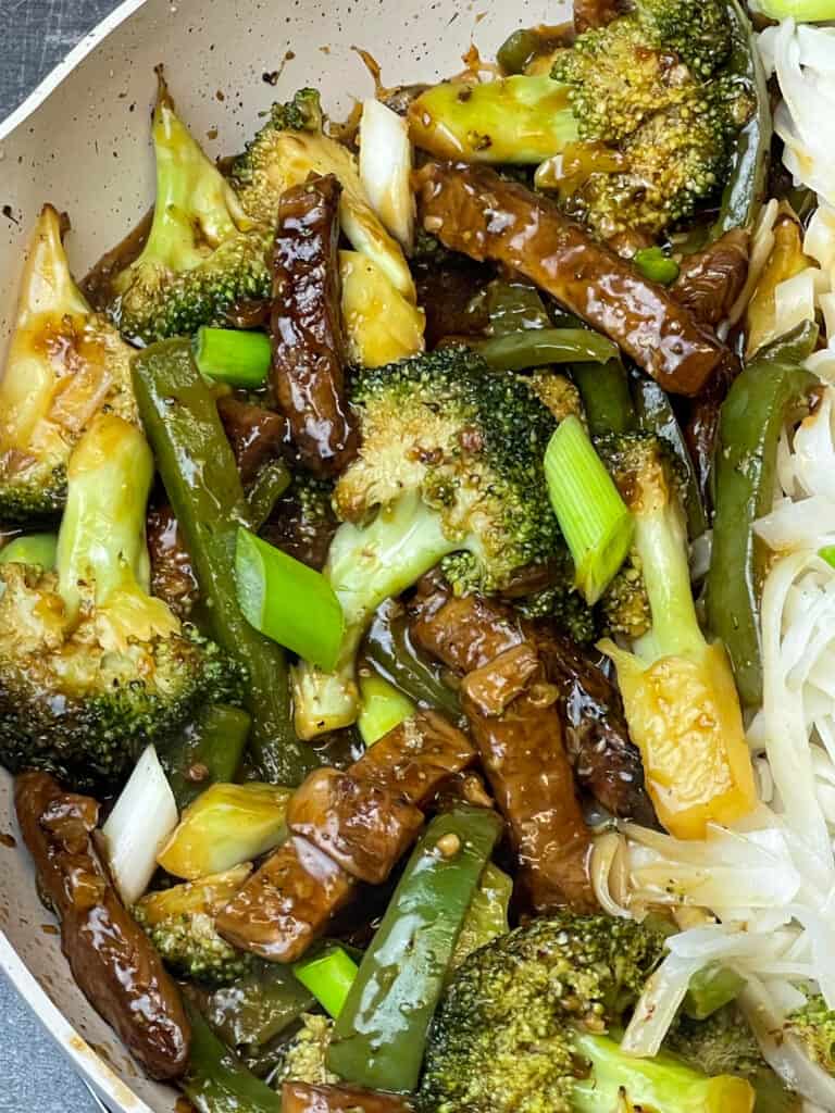 close up of wok full of Mongolian 'beef' and broccoli with spring onion garnish.