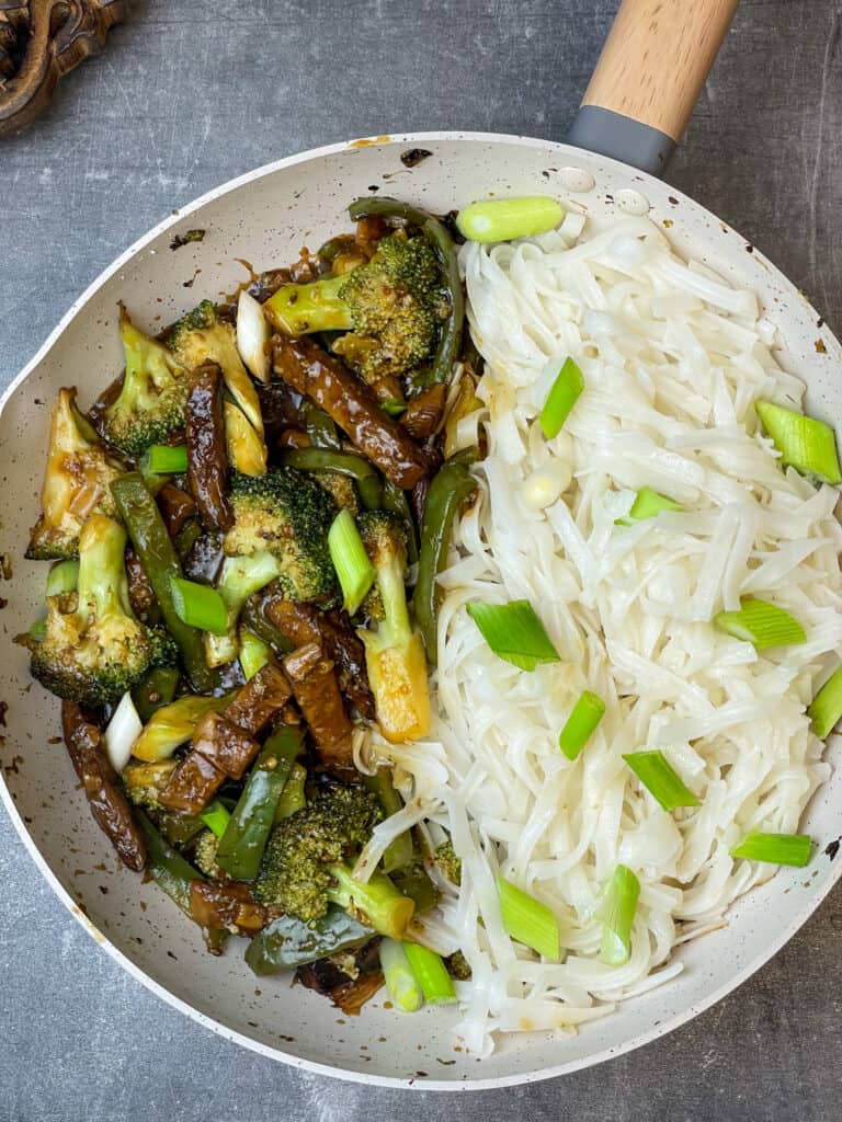 vegan Mongolian beef and broccoli cooked in grey and white wok with rice noodles and spring onion garnish, grey background, featured image.