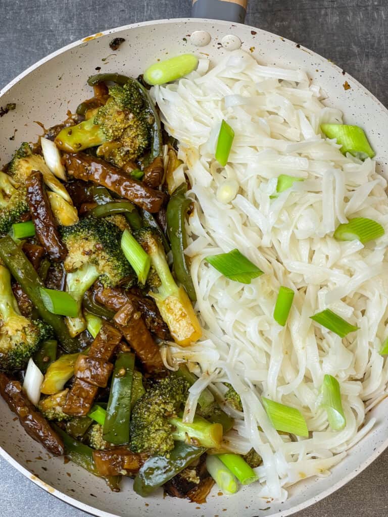 broccoli stir fry served with rice noodles and spring onion garnish.