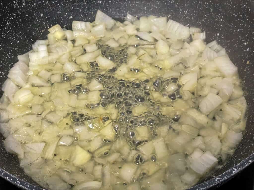 Veggie stock cooking onions and garlic for chickpea stew in black skillet pan.