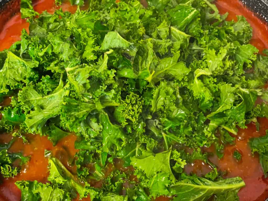 kale added to chickpea stew in skillet.