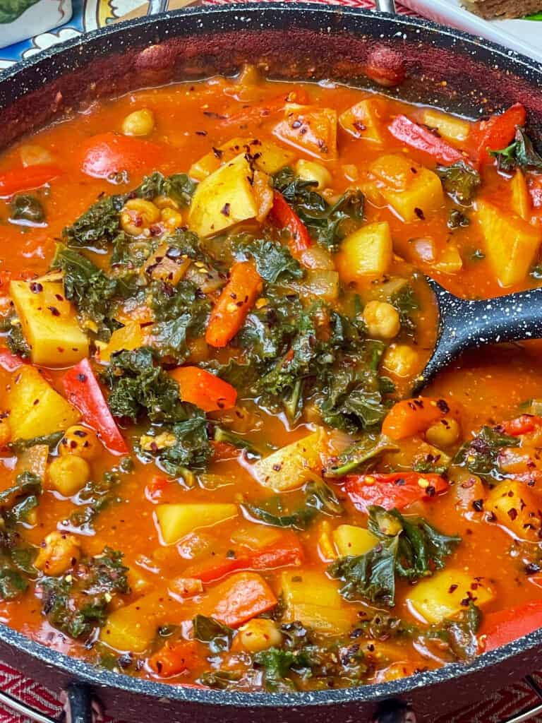 close up of vegan Spanish chickpea stew with ladle full of kale and stew.
