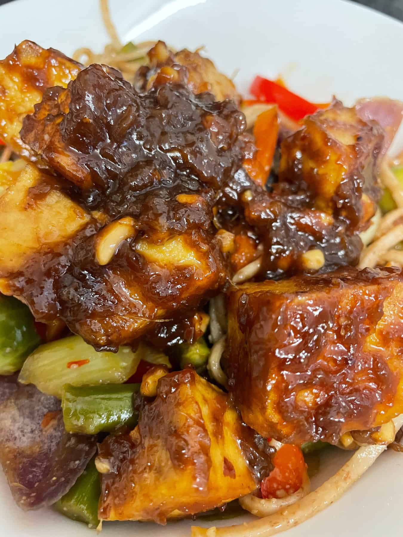 sweet peanut tofu served with stir fry veggies and noodles in white bowl, close up photo, featured image