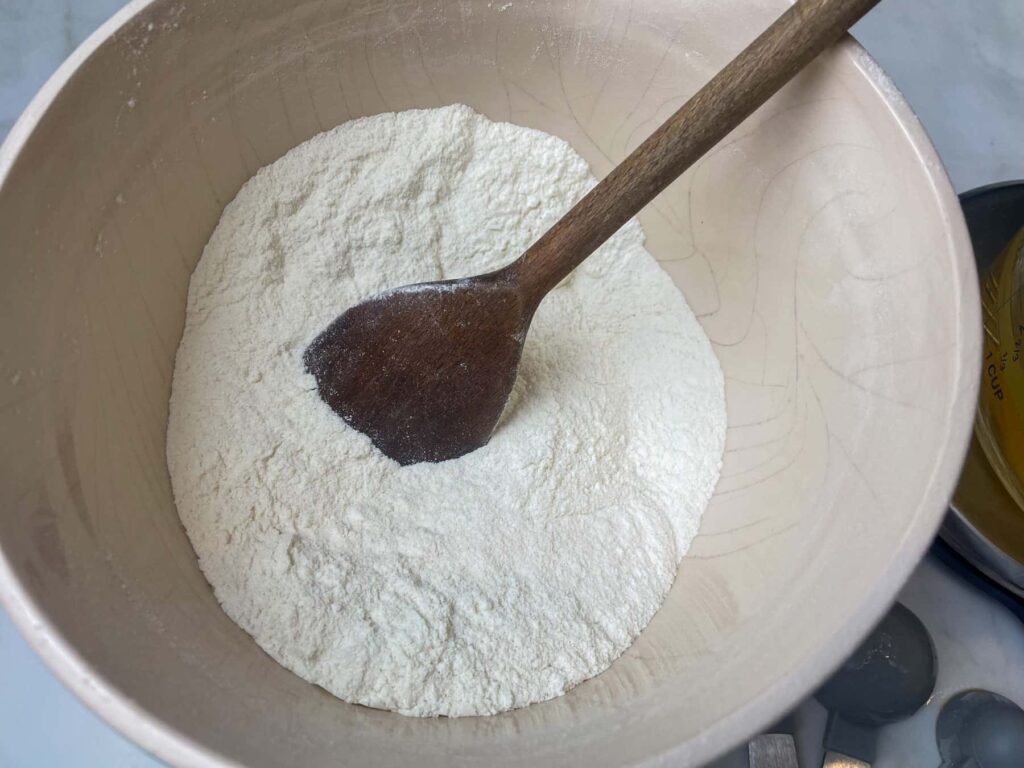 Dry ingredients added to mixing bowl with wooden spoon.