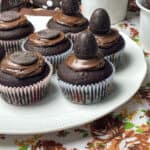 eggless chocolate wartime buns featured image, plate of chocolate buns decorated with choc spread and choc buttons and chocolate eggs, brown flour background.