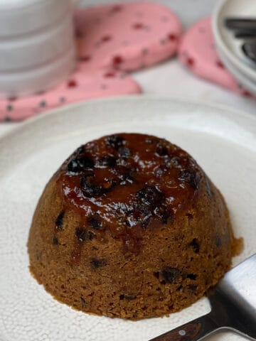 steamed date and syrup pudding on serving plate with jug of custard to side and pink oven mitt to side featured image.