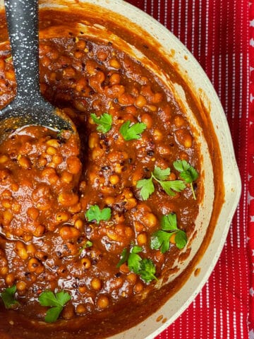 featured image for baked beans in tomato sauce, side view of pan full of beans garnished with parsley and ladle in pan, red background.