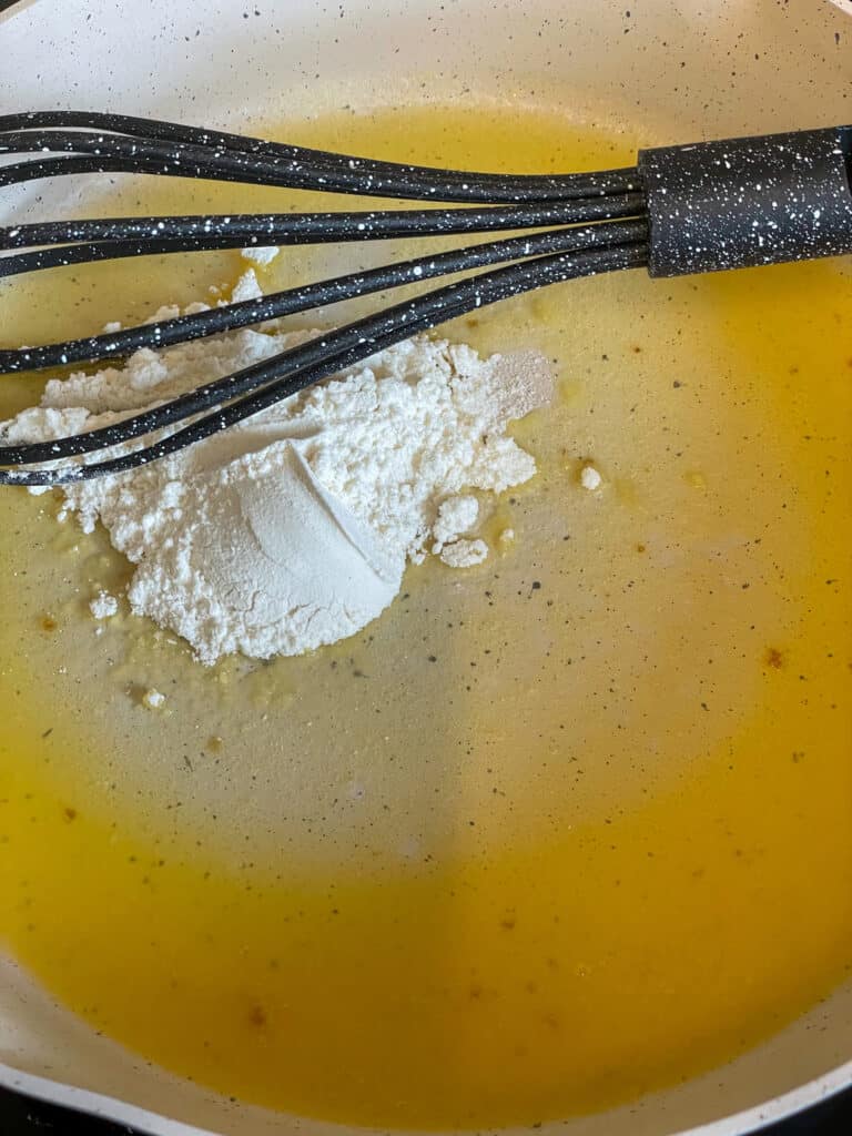 vegan margarine melted in cream coloured fry pan and flour added with black whisk ready to stir everything together into a flour roux.
