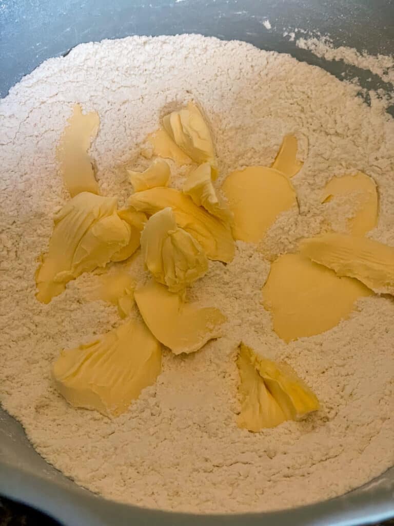 pieces of margarine added to flour, sugar and baking powder in turquoise mixing bowl.