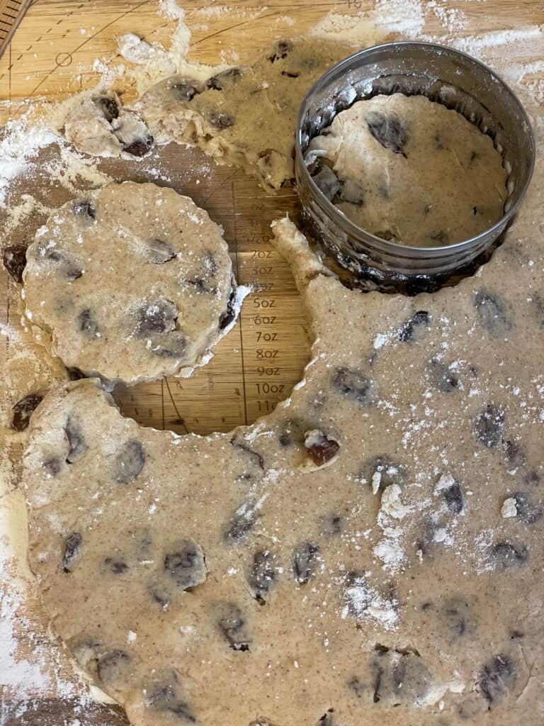 Welsh cake dough rolled out thin and stamped with biscuit cutter to create circles, on wooden chopping board.